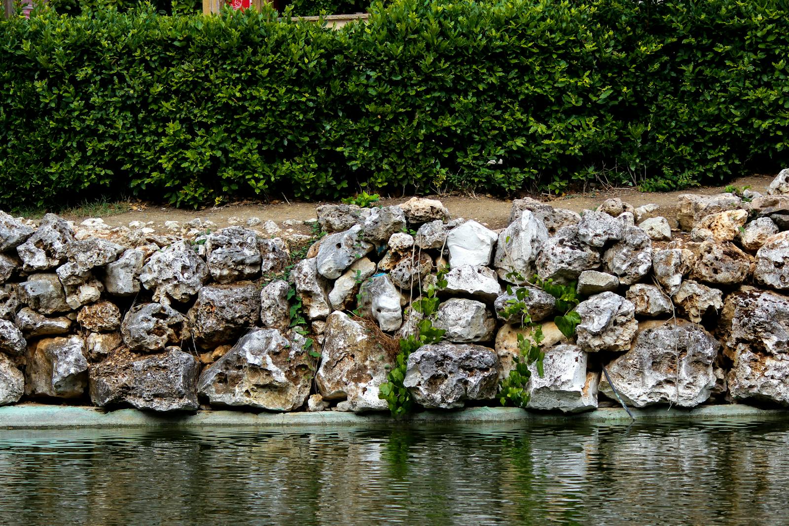 Limestone retaining wall framing a manicured planting bed and clipped hedge.
